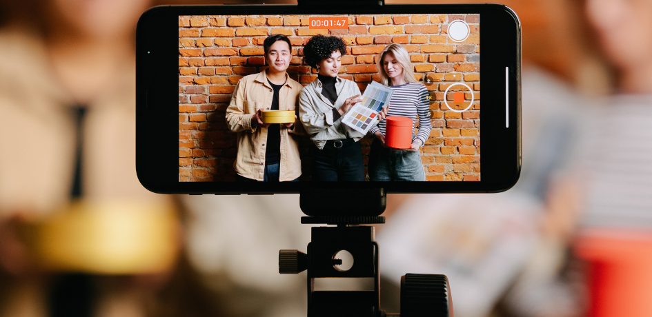Cellulaire qui filme 3 personnes en train de créer du contenu. Nous les voyons dans le cellulaire.
